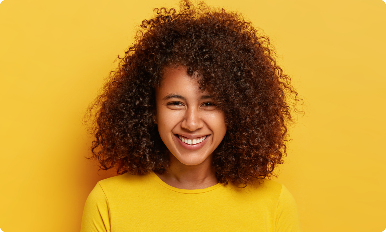 Femme aux cheveux bouclés souriant sur fond jaune