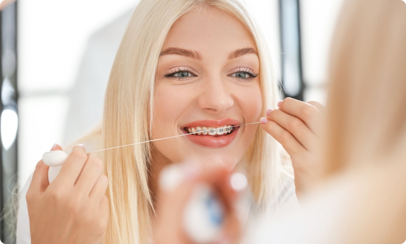 Femme souriante utilisant du fil dentaire devant un miroir