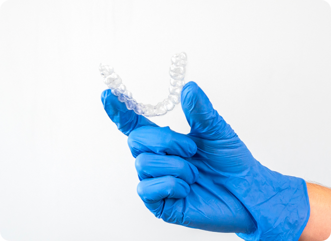 Gouttière orthodontique transparente tenue par une main gantée de bleu